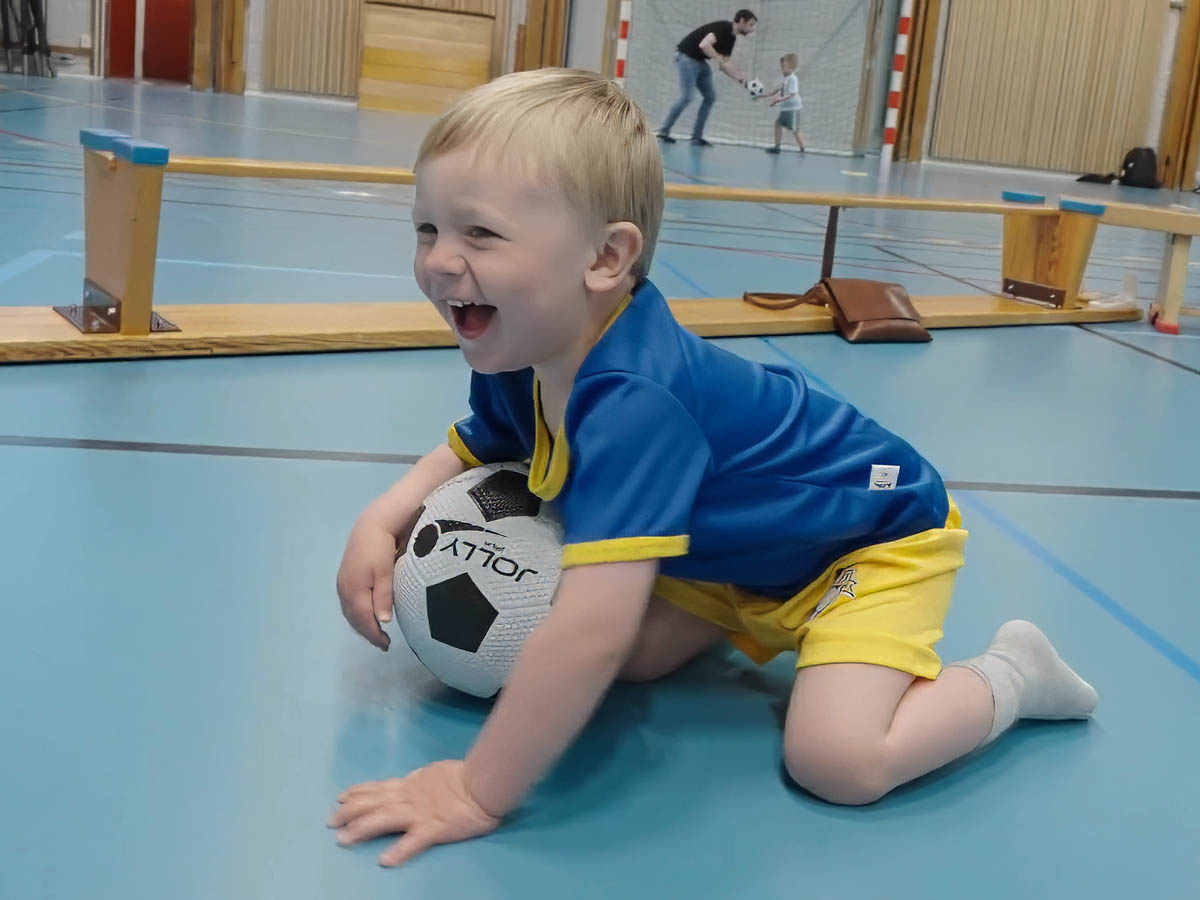 Glatt litet barn sitter med fotboll på Fotbollskul