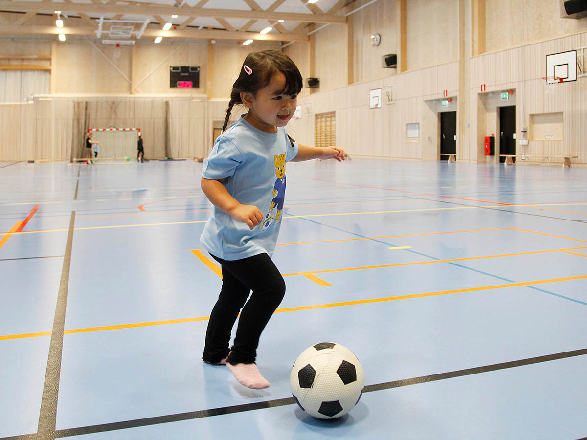 Ett barn sparkar fotboll i en idrottshall.