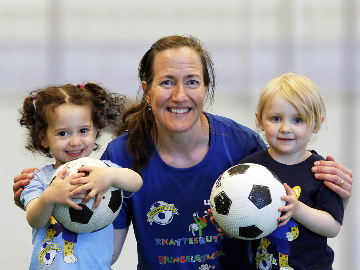 Ledare med två barn som håller fotbollar på Fotbollskul