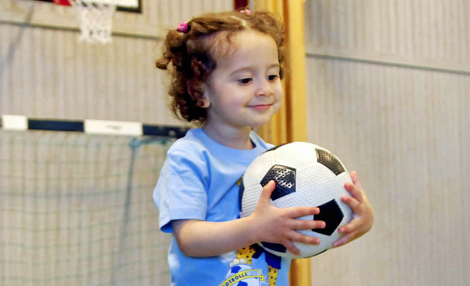 Barn håller en fotboll i idrottshall