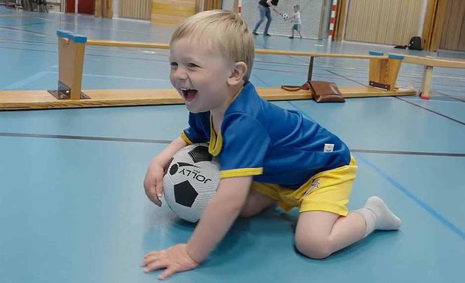 Glatt barn sitter med fotboll på Fotbollskul