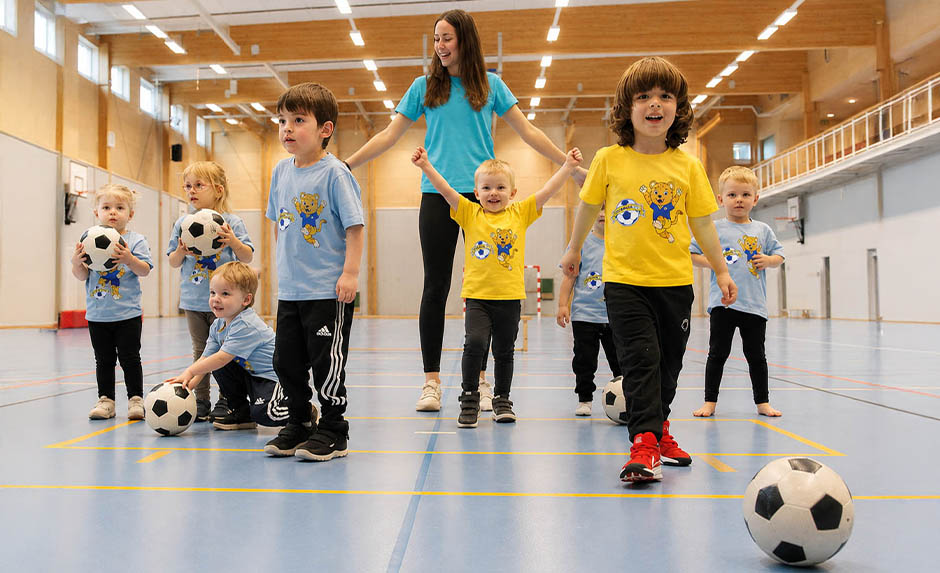 Barngrupp med fotbollar och ledare i idrottshall